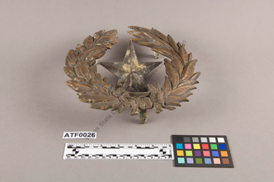 Star and wreath, 1850-1880. Artifacts Collection, ATF0026. TSLAC. Metal star and wreath, two pieces. Include mounting prongs for mounting on stone or wall. This Republic of Texas wreath and star (representative of the Texas state seal) were received from the Southwest Texas State College (present day Texas State University) in 1964 and are believed to have been embedded in cement over the entrance of the first Texas State Capitol building.